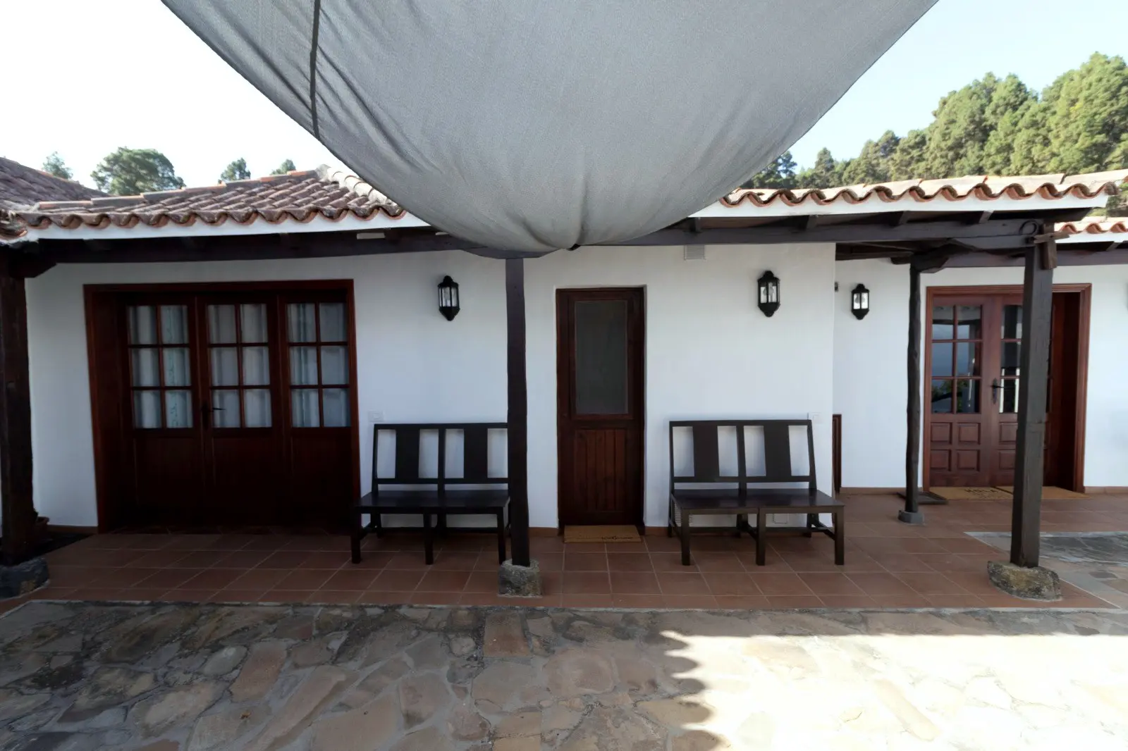 The porch at Finca Julia under an awning, with a tiled roof, wooden benches and the midland pine forest behind