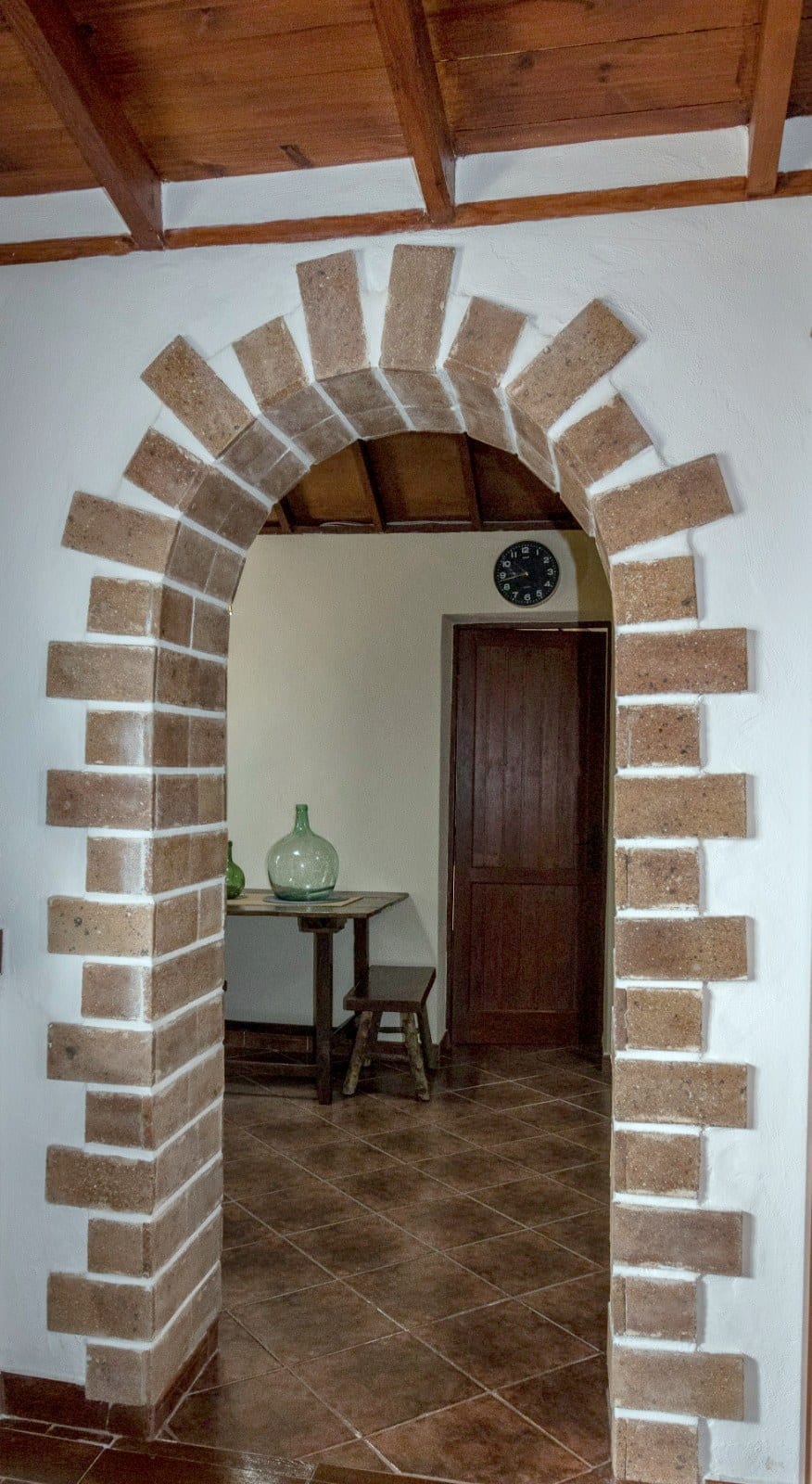 Arco de ladrillo visto sobre pared encalada en el interior de Finca Julia, bajo un techo de vigas de madera