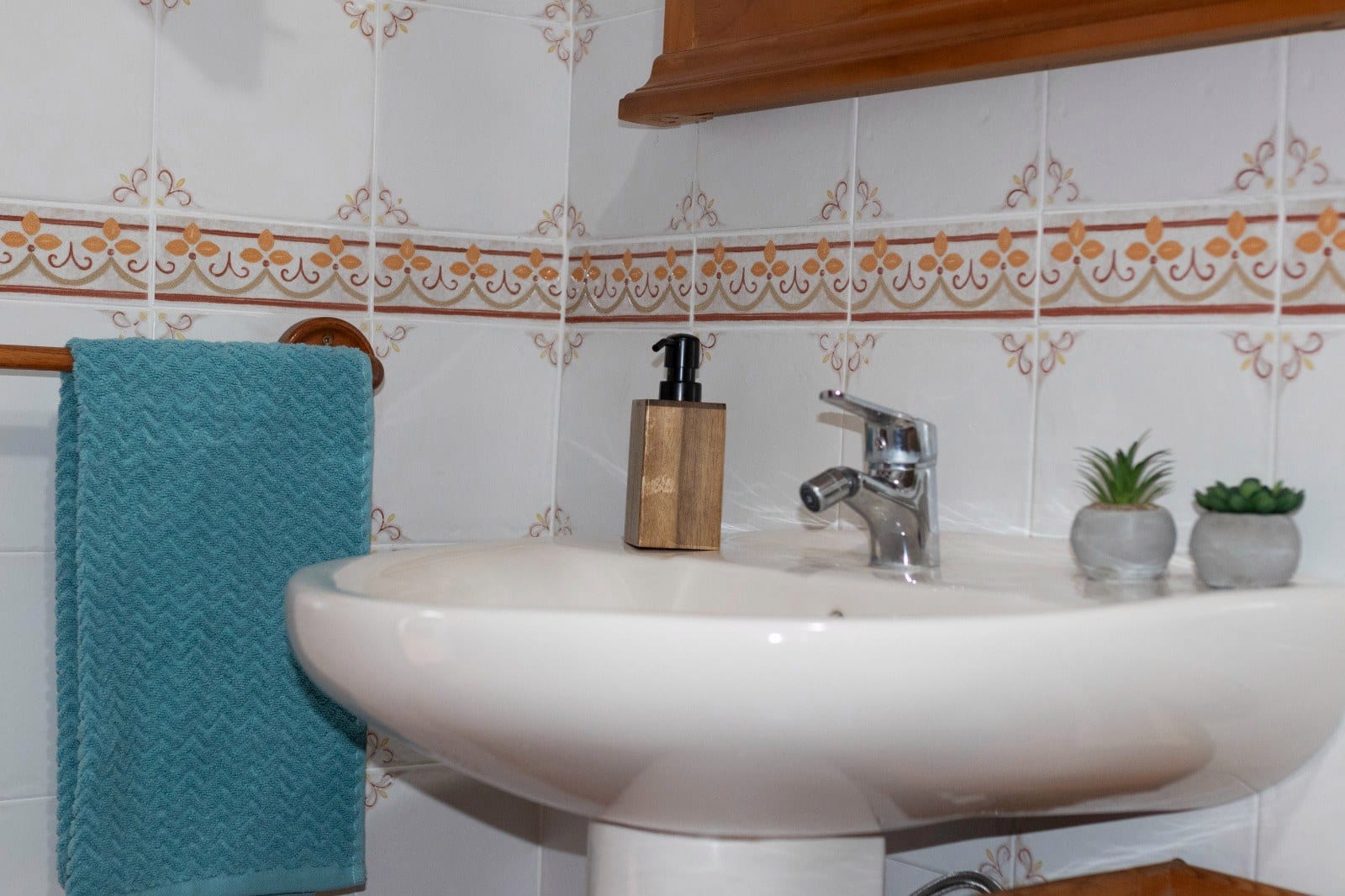Lavabo del baño de Finca Julia con azulejo tradicional de cenefa pintada, toalla y dosificador de madera