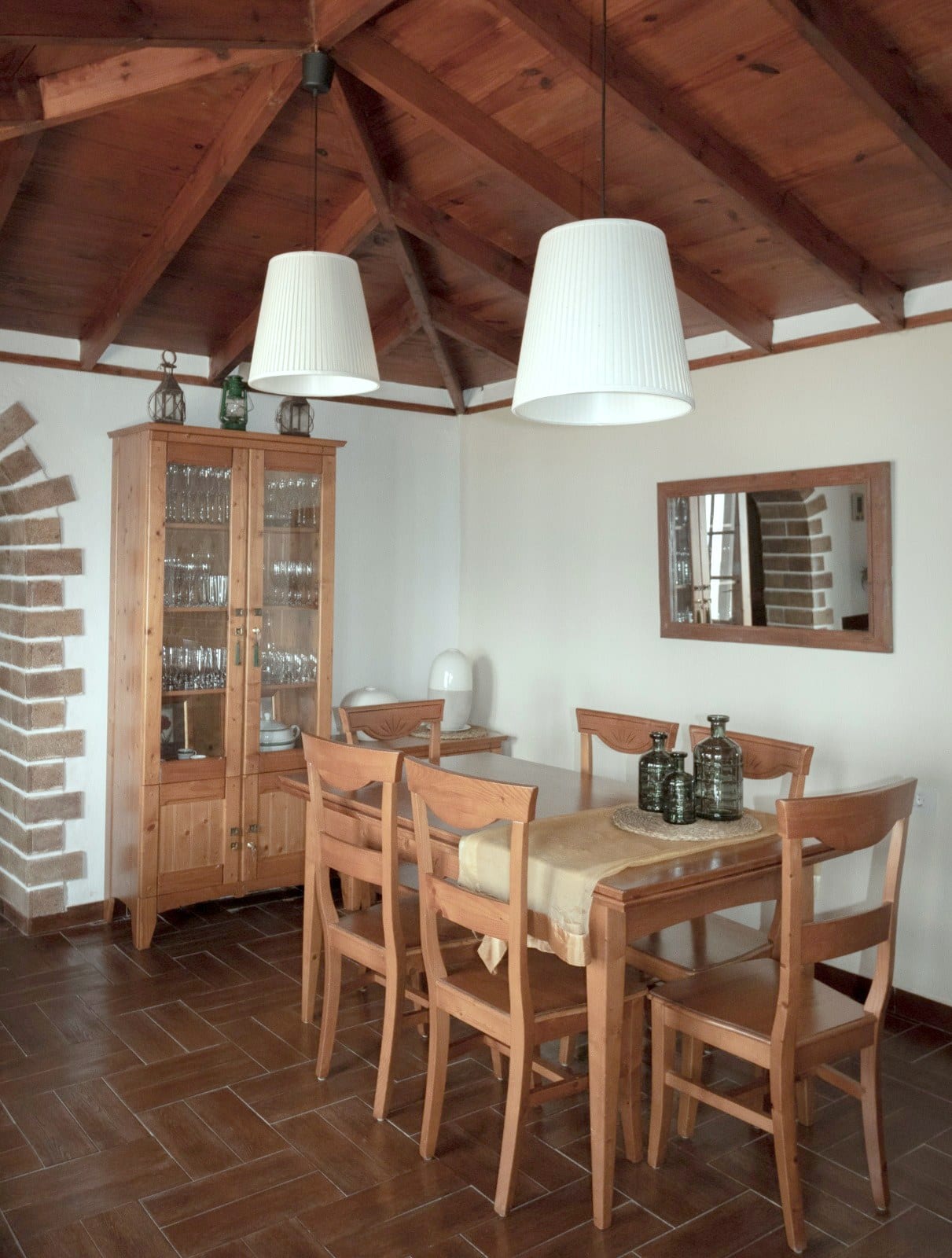 Comedor de Finca Julia con mesa y seis sillas de madera, vitrina con cristalería y techo de vigas vistas