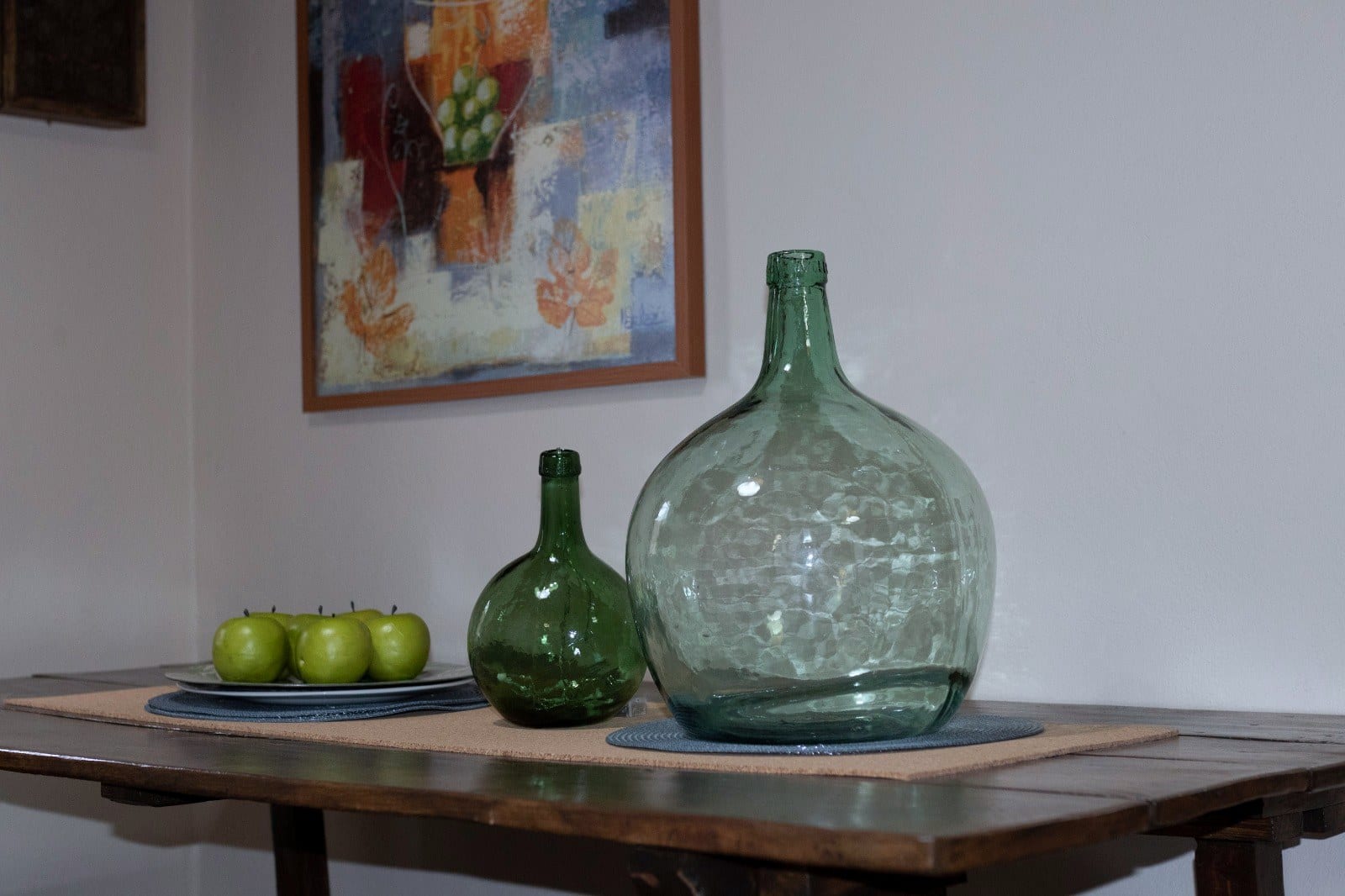 Dos damajuanas de vidrio verde y un plato de manzanas sobre la mesa de madera maciza de Finca Julia