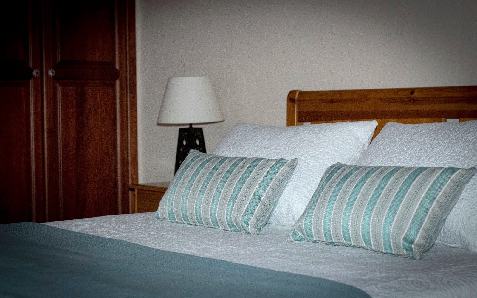Detalle del cabecero de madera y los cojines de rayas de un dormitorio de Finca Julia, con el armario al fondo