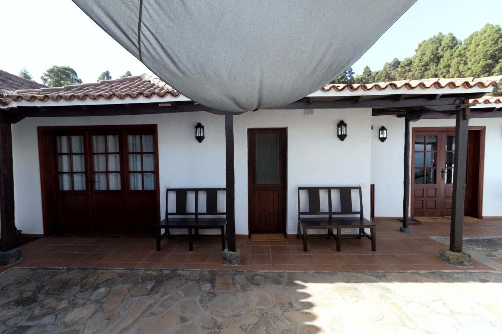 Porche de Finca Julia bajo un toldo, con tejado de teja, bancos de madera y el pinar de las medianías detrás